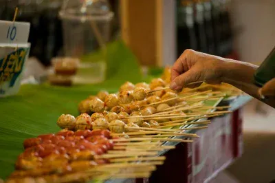 A hand selects skewers at a vibrant Thai street food market, highlighting local culinary culture.